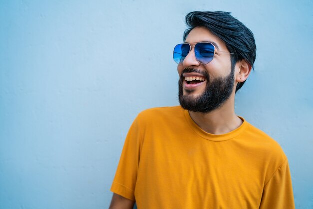 Portrait of young handsome man wearing summer clothes and sunglasses against blue space.