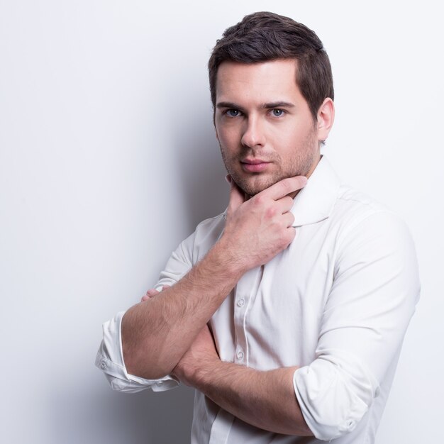 Portrait of young handsome man in white shirt poses over wall with contrast shadows.