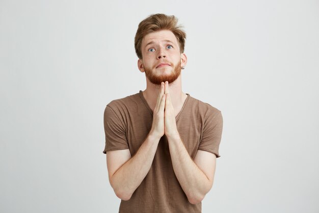 Portrait of young handsome man with beard praying hoping.