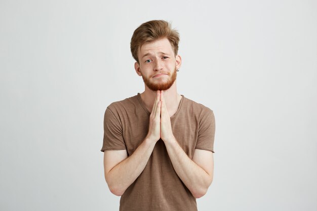 Portrait of young handsome man with beard praying hoping.