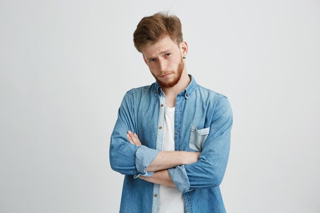 Portrait of young handsome man with crossed arms raising up brow looking at camera.