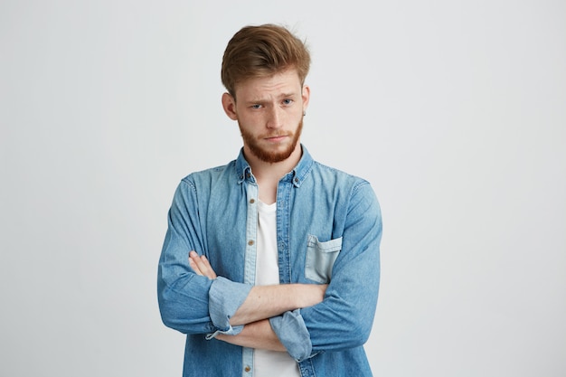 Portrait of young handsome man with crossed arms raising up brow looking at camera.