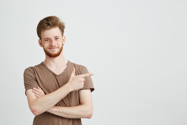 Portrait of young handsome sincere man with beard smiling pointing finger in side.