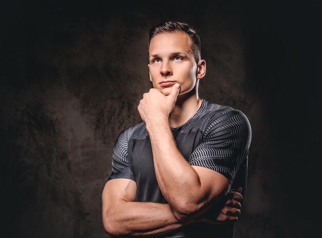 Portrait of a young handsome sportsman holds hand on chin on a dark background.