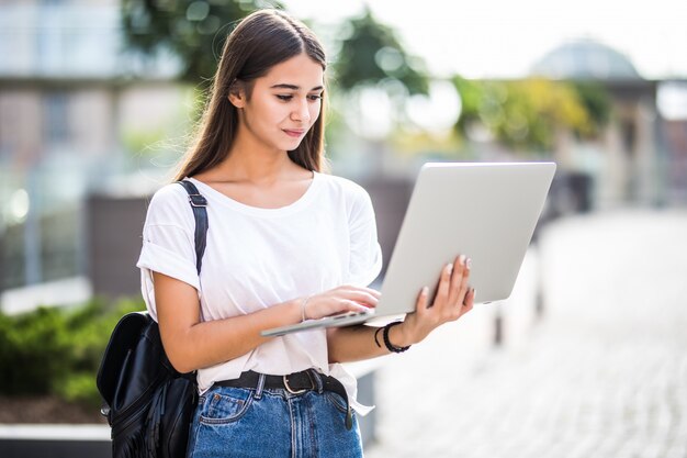 Портрет молодого счастливого блоггера с современным ноутбуком на открытом воздухе