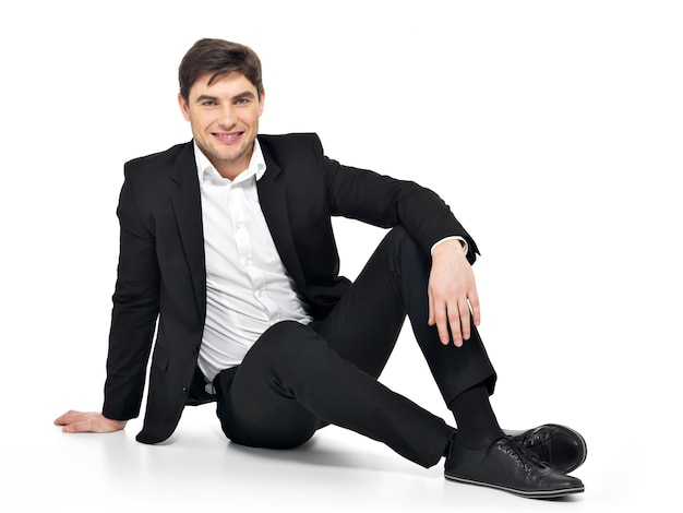 Portrait of young happy businessman sitting on floor isolated on white. 
