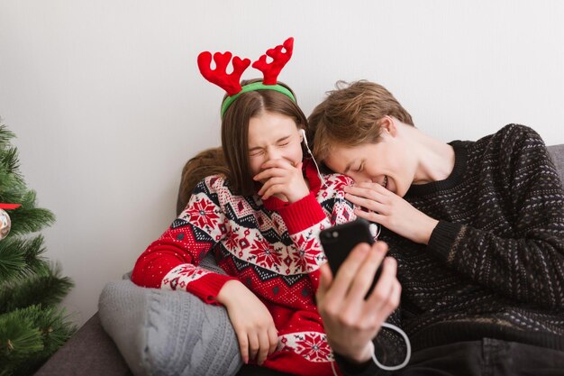 Portrait of young happy couple sitting on sofa at home and listening music while spending time together