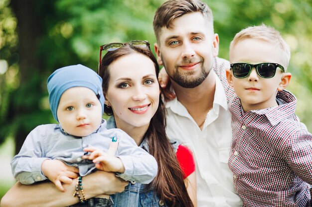 Free photo portrait of young happy family wearing in casual outfits spending time together at park man and woman kissing his little son boys looking and smiling at camera