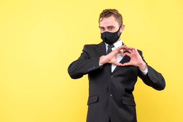 Portrait of young happy guy showing heart shape with hands on yellow