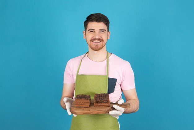 青にチョコレートケーキのスライスを持つ若い幸せな男の肖像画。