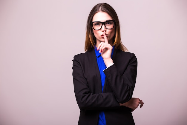 Free photo portrait of young happy smiling business woman keeping finger on her lips and asking to keep quiet, isolated over white wall