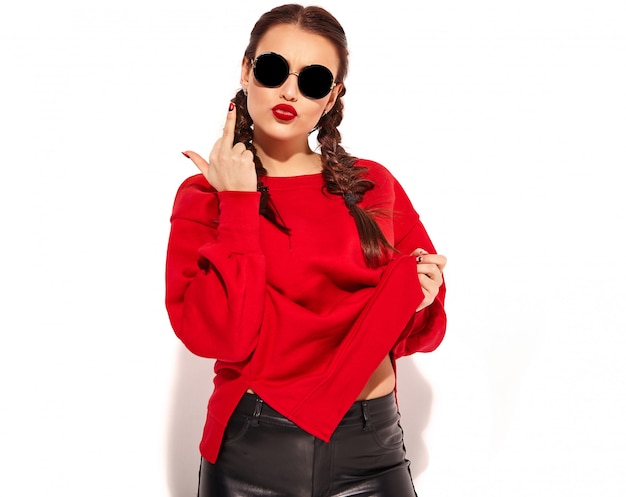 Portrait of young happy smiling woman model with bright makeup and colorful lips with two pigtails and sunglasses in summer red clothes isolated. showing fuck off sign