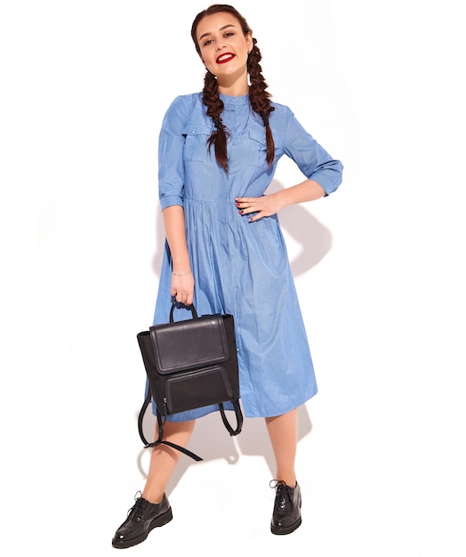 Portrait of young happy smiling woman model with bright makeup and red lips with two pigtails in hands in summer colorful blue dress and backpack isolated.