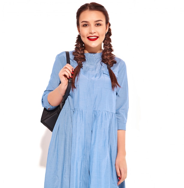 Portrait of young happy smiling woman model with bright makeup and red lips with two pigtails in hands in summer colorful blue dress and backpack isolated