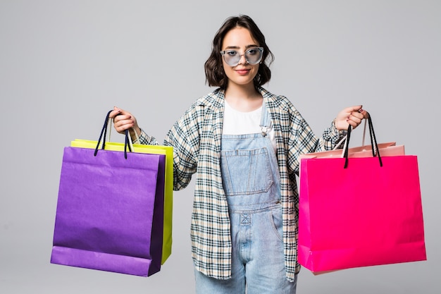 Portrait of young happy smiling woman in sunglasses with shopping bags isolated on gray. Sale concept.