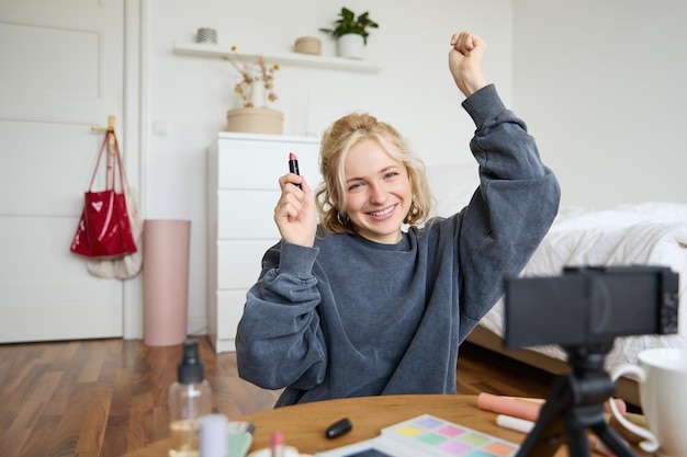 Free photo portrait of young happy woman content media creator recording a vlog about makeup in her room using