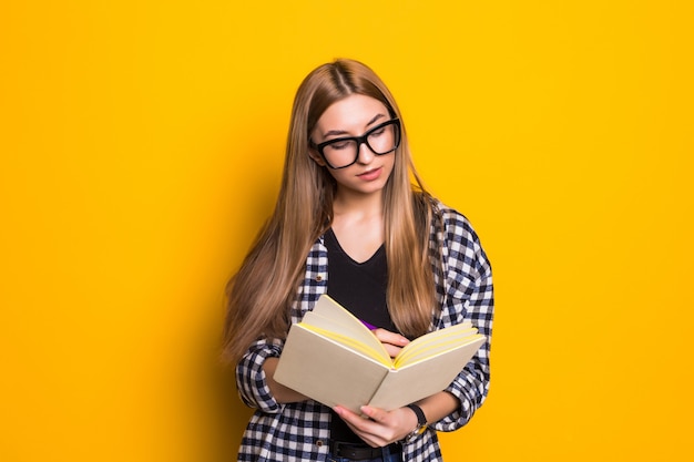 Ritratto giovane donna felice lettura libro educazione studiando apprendimento conoscenza sorridente emozione positiva nel muro giallo