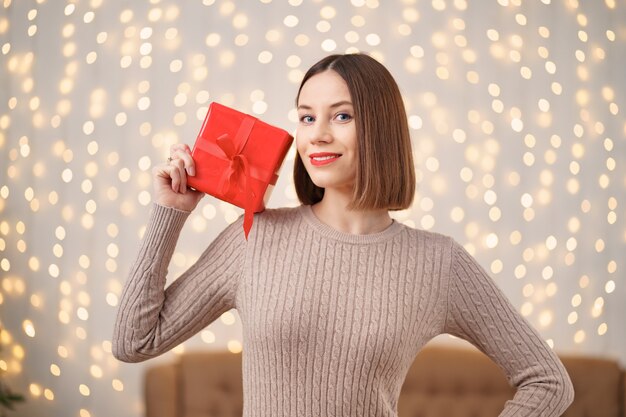 Портрет молодой счастливой женщины красные губы держа обернутую подарочную коробку.
