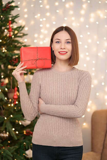 Портрет молодой счастливой женщины с красными губами, глядя в камеру, держа обернутую подарочную коробку