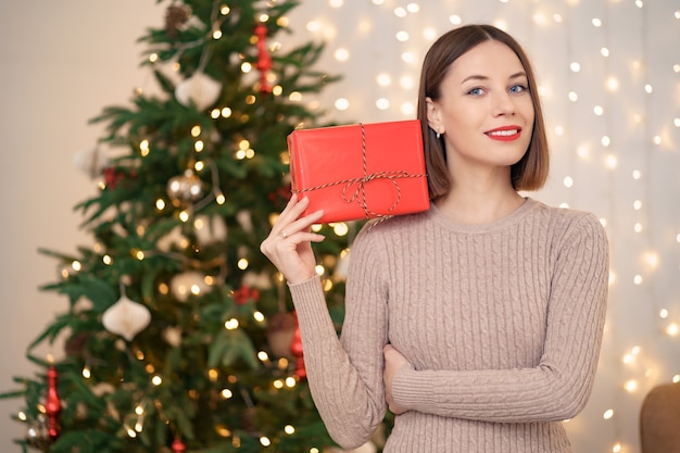 Ritratto di giovane donna felice labbra rosse che guarda l'obbiettivo che tiene una confezione regalo avvolta