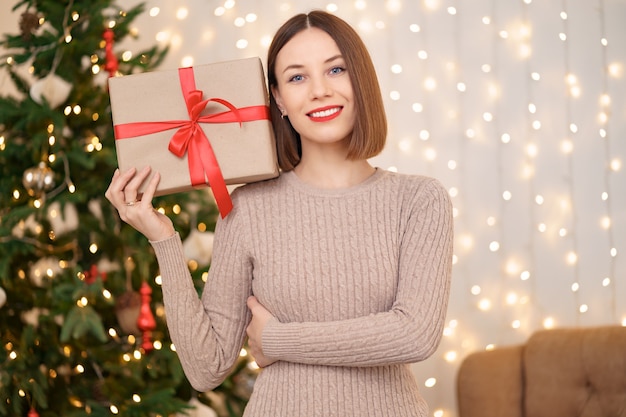 Portrait of young happy woman red lips looking at camera holding a wrapped gift box.