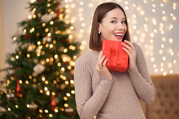 Portrait of young happy woman red lips posing with a wrapped gift box.