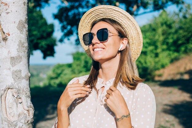 Портрет молодой счастливой женщины в солнцезащитных очках и соломенной шляпе