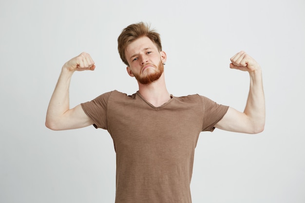 Portrait of young healthy sportive man showing biceps muscles boasting looking at camera.