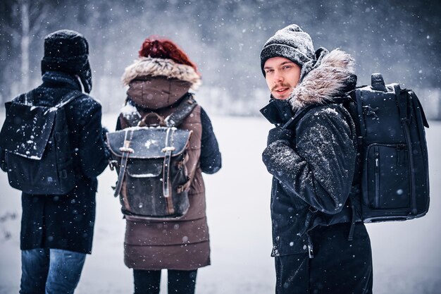 Портрет молодого туриста с рюкзаком, идущего с друзьями по зимнему лесу