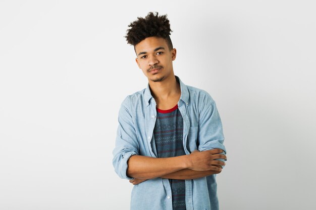 Portrait of young hipster black man posing on isolated white studio wall background, stylish outfit, funny afro hairstyle, confident, arms crossed on chest, serious