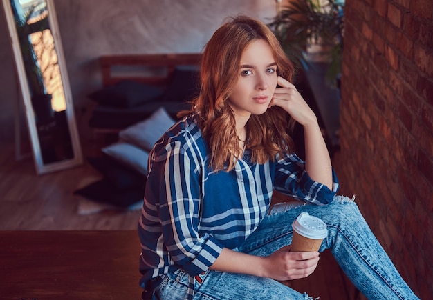 Portrait of a young hipster girl drinks morning coffee sits on a