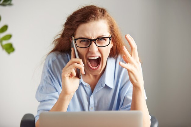 Portrait of a young irritated businesswoman wearing glasses and shirt looking with anger