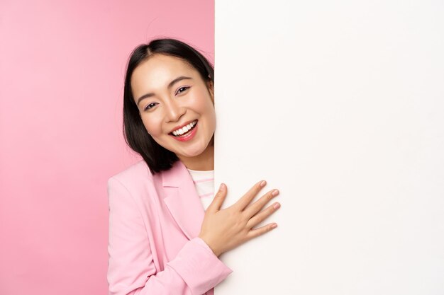 Portrait of young japanese business woman corporate lady in suit pointing on wall with chart showing diagram or advertisement on empty copy space pink background