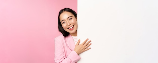 Ritratto di giovane donna d'affari giapponese donna corporativa in tuta che punta sul muro con diagramma che mostra diagramma o pubblicità su sfondo rosa spazio vuoto copia