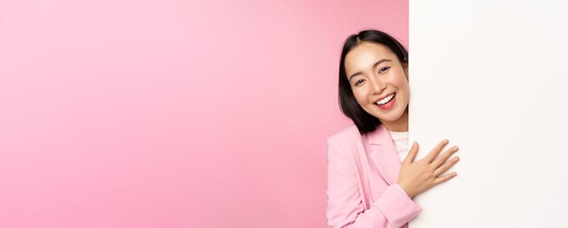 空のコピースペースピンクの背景に図や広告を示すチャートで壁を指しているスーツの若い日本のビジネス女性企業の女性の肖像画