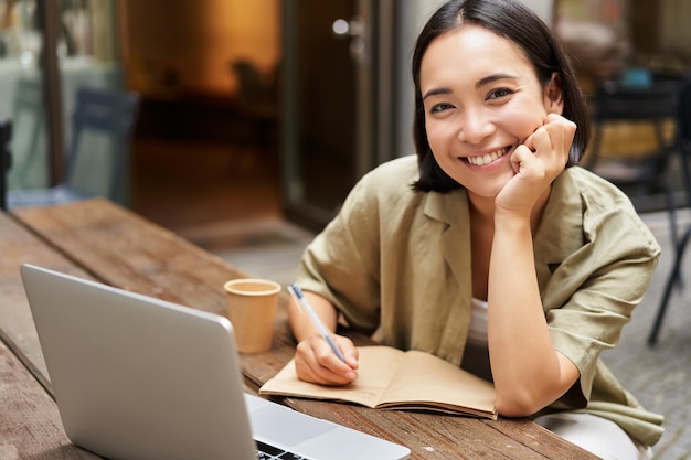 Free photo portrait of young korean girl making notes listening online meeting lecture looking at laptop screen