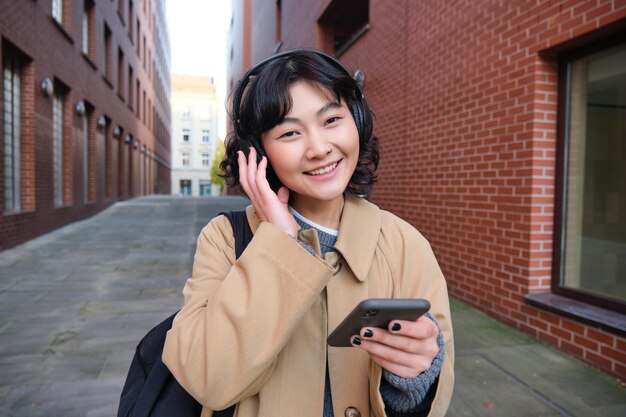 배낭과 헤드폰을 들고 도시를 돌아다니는 젊은 한국 여성의 초상화는 음악을 듣는다