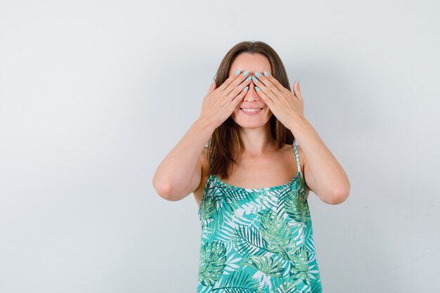 Portrait of young lady covering eyes with hands in blouse and looking happy front view