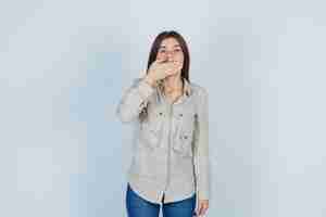 Free photo portrait of young lady covering mouth with hand in casual, jeans and looking shocked front view