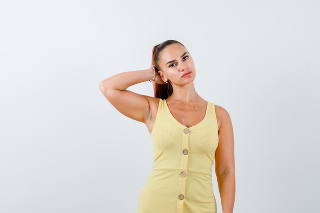 Portrait of young lady holding hand behind head in yellow dress and looking sensible front view