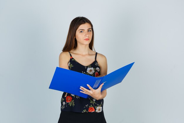 Portrait of young lady holding opened folder in blouse and looking pensive front view