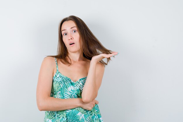 Portrait of young lady holding strand of hair in blouse and looking puzzled front view