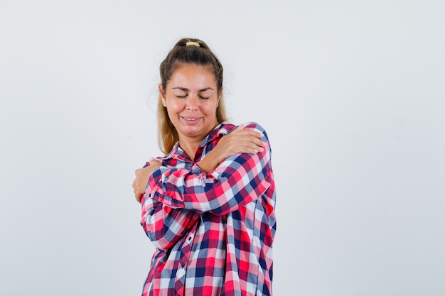 Free photo portrait of young lady hugging herself in checked shirt and looking charming front view