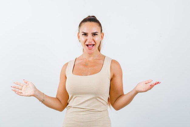 Portrait of young lady keeping arms wide spread in beige tank top and looking happy front view