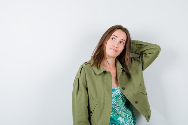 Portrait of young lady keeping hand behind head in blouse, jacket and looking pensive front view