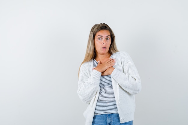 Ritratto di giovane donna tenendo le mani sul petto in t-shirt, giacca e guardando spaventato vista frontale