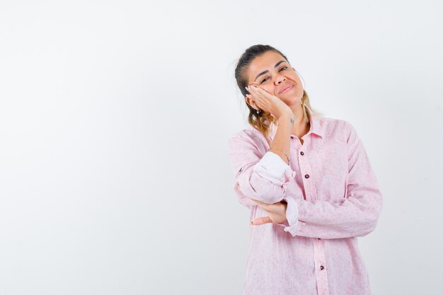 Portrait of young lady leaning cheek on raised palm in pink shirt and looking cute front view