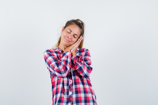 Portrait of young lady leaning on palms as pillow in checked shirt and looking peaceful front view