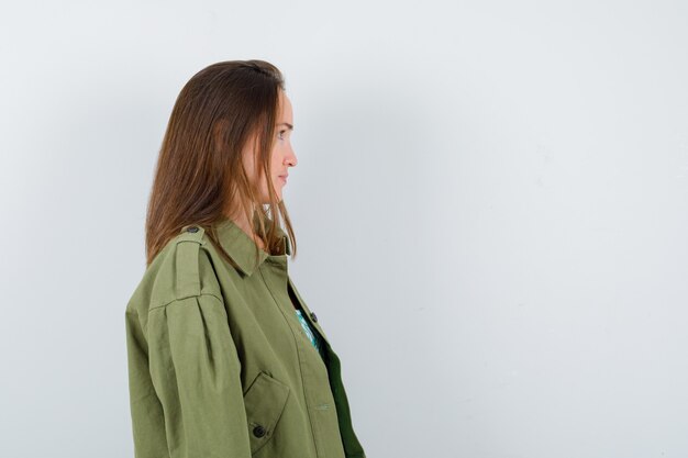 Портрет молодой леди, смотрящей в сторону, стоящей боком в зеленой куртке и выглядящей сосредоточенной