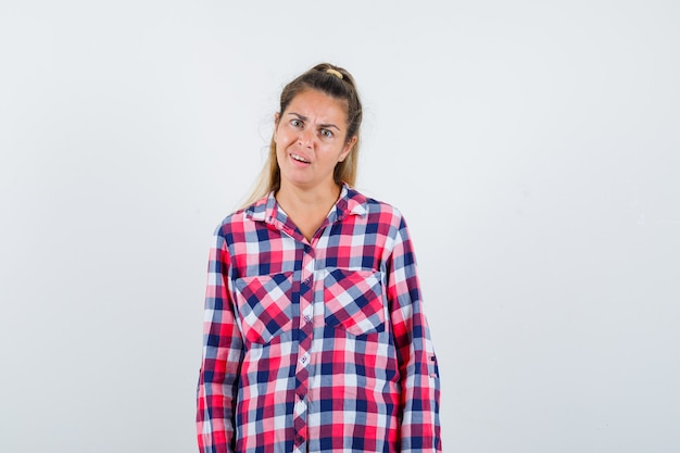 Portrait of young lady looking at camera in checked shirt and looking confused front view